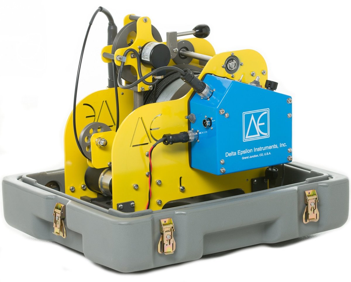 Delta Epsilon portable borehole logger: a yellow winch frame with cable drum and hand crank, fitted with a blue Delta Epsilon Instruments control module, mounted inside a gray latched transport case